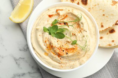 Kırmızı biberli leziz humus, beyaz mermer masada pide ve limon.