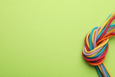Açık yeşil arkaplanda düğümlenmiş renkli ipler, metin için yeri olan üst görünüm. Birlik kavramı