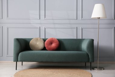 Gri duvarın yanında rahat bir kanepe ve lamba.