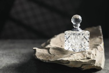 Gri masada bir şişe parfüm ve taş, metin için yer.