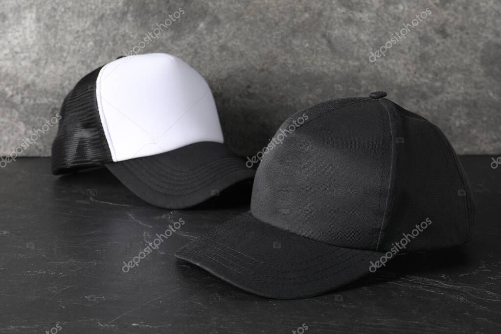 Stylish baseball caps on dark textured table. Mockup for design