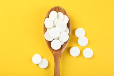 Sarı arka planda kaşıkta antibiyotik haplar, üst manzara.