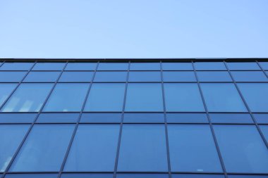 Açık mavi gökyüzüne karşı birçok penceresi olan modern binanın dış görünüşü, düşük açı görünümü