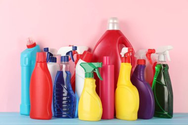 Açık mavi ahşap masada pembe arka planda farklı temizlik ürünleri