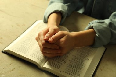İngilizce İncil 'i açık olan kadın bej masada dua ediyor, yakın plan.