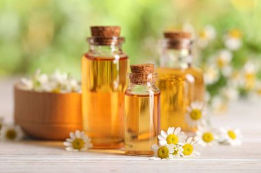 Beyaz ahşap masada, bulanık arka planda, yakın planda, gerekli yağ ve papatya çiçekleri.