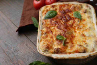 Ahşap masada fesleğen ve fırında pişirilmiş nefis lazanya, yakın plan. Metin için boşluk