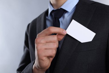Gri arka planda ceketinin cebinden boş kartvizit alan adam, yakın plan. Tasarım için model