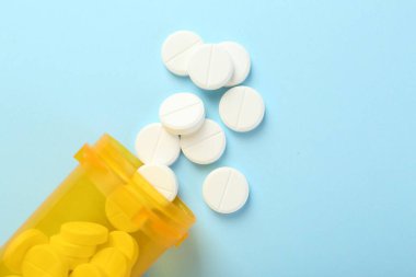 Açık mavi arka planda bir şişe antibiyotik hapı.