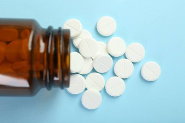 Açık mavi arka planda bir şişe antibiyotik hapı.