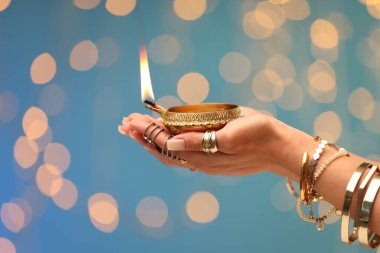 Diwali kutlaması. Açık mavi arka planda yanan diya lambasını tutan bulanık ışıklı kadın, yakın plan.