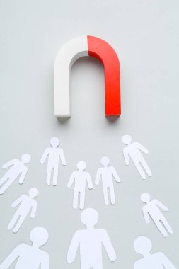 Mıknatıs, açık gri arka planda, düz zeminde insanların kağıt kesiklerini çekiyor.