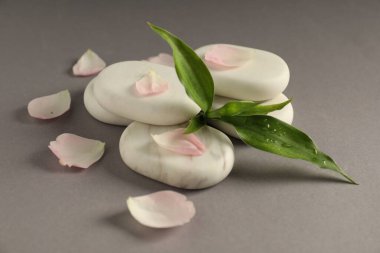 Spa taşları, taç yaprakları ve yeşil yapraklar gri masada, yakın plan.