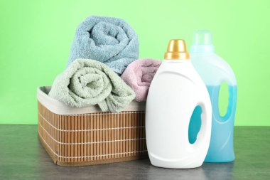 Çamaşır deterjanı şişelerde ve havlular gri masada.