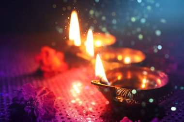 Mutlu Diwali kutlamaları. Diya lambaları yanıyor ve arka planda güzel çiçekler, yakın plan. Bokeh etkisi