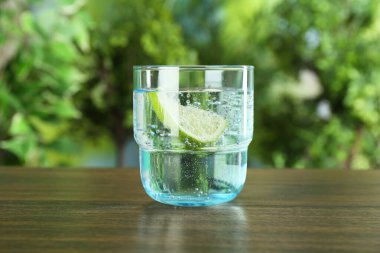 Bir bardak limonlu soda, ahşap masada bulanık arka planda.