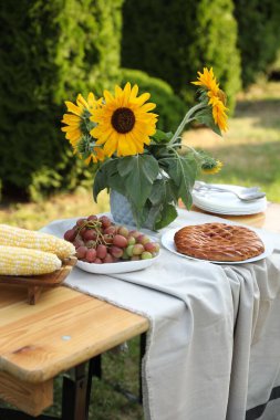 Bahçedeki ahşap masada vazo, üzüm, turta ve mısır koçanı.
