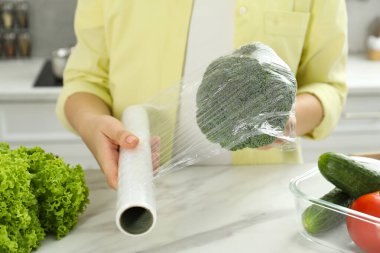 Kadın mutfaktaki tezgahta brokoliyi plastik gıda ambalajıyla kaplıyor.