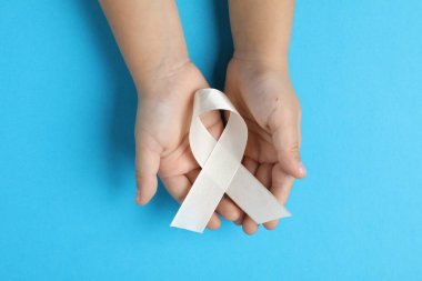 Açık mavi arka planda beyaz kurdeleli bir çocuk. Kemik kanseri ve akciğer hastalığı farkındalığı