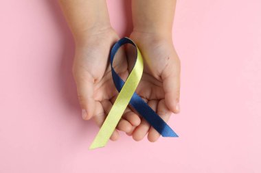 Pembe arka planda sarı ve mavi kurdeleli bir çocuk. Down sendromu farkındalığı