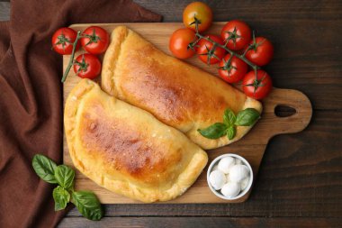 Lezzetli vejetaryen calzones fesleğenli, mozzarella peynirli ve domatesli ahşap masa, üst görünüm