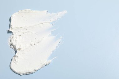 Açık mavi arka planda krem izleri, yakın plan. Metin için boşluk