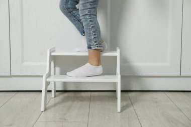 Little girl standing on step stool indoors, closeup clipart