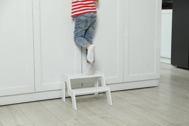 Little girl standing on step stool indoors, closeup clipart