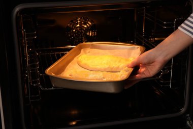 Yanmamış calzone pizzayla tabağı fırına koyan kadın, yakın plan.