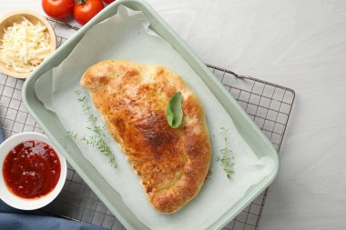 Lezzetli calzone pizzası fırın kabında ve malzemeler beyaz ahşap masada, düz yerde.