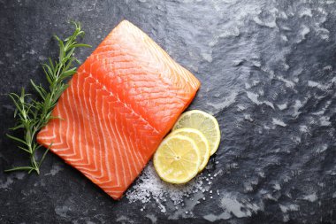 Bir parça taze somon, limon ve biberiye, koyu masa, üst manzara. Metin için boşluk