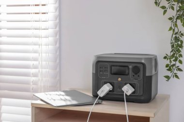 İçerideki ahşap masada taşınabilir elektrik santralinden dizüstü bilgisayar şarj ediliyor.