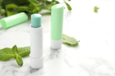 Beyaz mermer arka planda doğal dudak kremleri ve nane yaprakları, yakın plan. Metin için boşluk