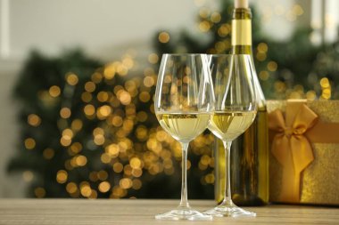 Ahşap masada, bulanık Noel ışıklarına karşı, bardaklar ve bir şişe beyaz şarap. Metin için boşluk