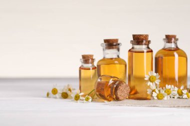 Beyaz ahşap masa üzerinde gerekli yağ ve papatya çiçekleri, yakın plan. Metin için boşluk