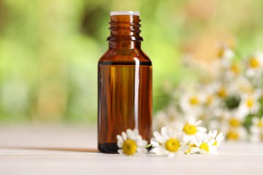 Beyaz ahşap masada, bulanık arka planda, yakın planda, gerekli yağ ve papatya çiçekleri.