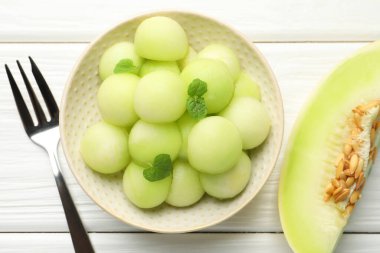 Melon balls in bowl and fresh fruit on wooden table, top view clipart