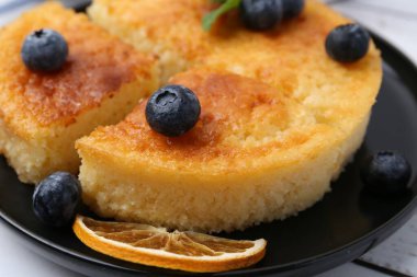 Delicious semolina cake with blueberries and orange slices on white wooden table, closeup clipart