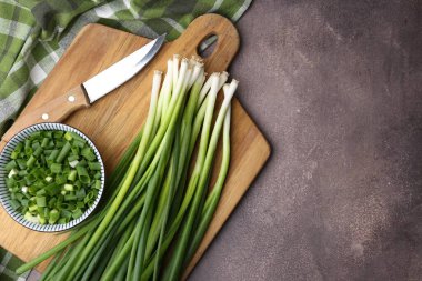 Kavanozda doğranmış yeşil soğan, saplar ve bıçak kahverengi masada, üst tarafta. Metin için boşluk
