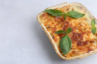 Delicious cooked lasagna in baking dish and basil on light grey table, closeup. Space for text clipart