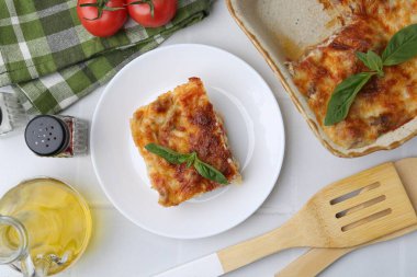 Beyaz masada servis edilen fesleğenli lezzetli pişmiş lazanya.