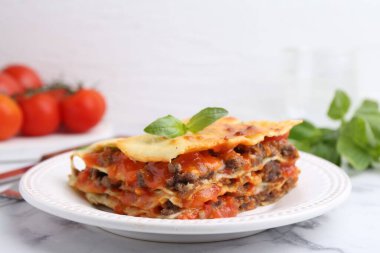 Lezzetli pişmiş lazanya, fesleğen ve beyaz mermer masa, yakın plan.