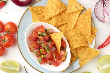 Lezzetli salsa (Pico de gallo) beyaz ahşap masadaki ürünler arasında nachos ile servis edilir.