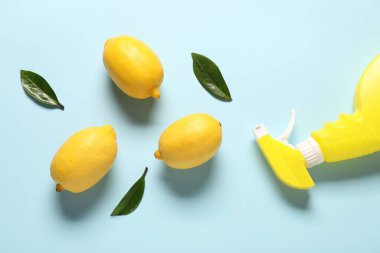Açık mavi arka planda bir şişe temizlik malzemesi ve limonlar.