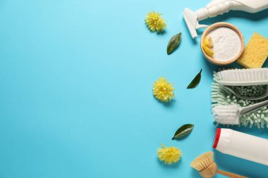 Açık mavi arka planda temizlik ürünleri, aletler ve çiçekler, düz yatak. Metin için boşluk