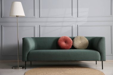 Gri duvarın yanında rahat bir kanepe ve lamba.