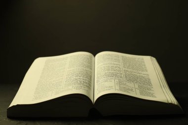 Open Holy Bible in English language on black table, closeup clipart