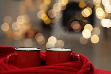 Fincanlarda lezzetli kakao ve arka planda bulanık kırmızı eşarp, yakın plan. Noel içeceği