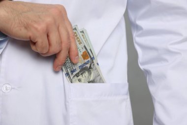 Yozlaşma konsepti. Doktor, gri arka planda cebine dolar banknotları koyuyor.