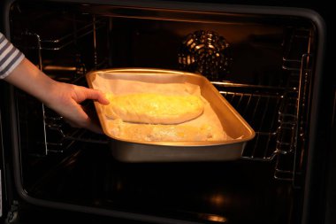 Yanmamış calzone pizzayla tabağı fırına koyan kadın, yakın plan.